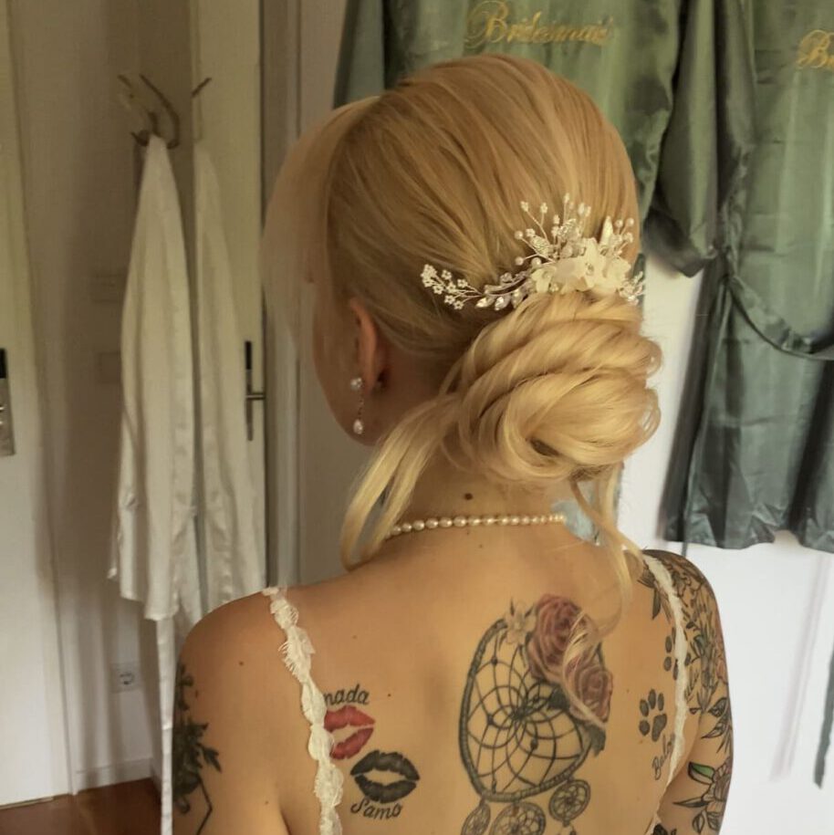 Braut mit elegantem, tiefem Knoten und floralem Haarschmuck in Spitzenkleid, romantisches Hochzeitsstyling.