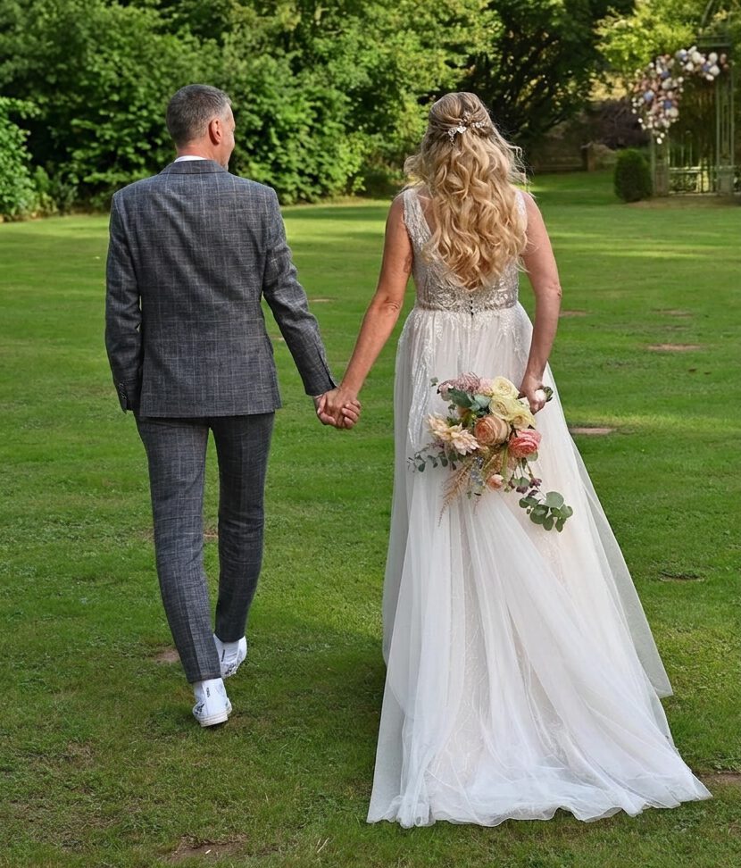 Rückenansicht Braut im Pakr in den Weyberhöfen Sailauf bei Aschaffenburg, halboffene Brautfrisur, volumige Locken, Brautstrauß, blumiger Haarschmuck